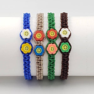 Peut inclure: Quatre bracelets d'amitié colorés avec des breloques de fleurs souriantes. Les bracelets sont faits de cordon tressé en bleu, beige, vert et marron.