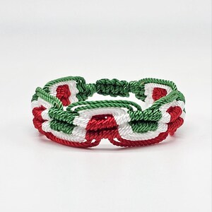May include: A green, white, and red braided friendship bracelet. The bracelet is made of woven string and has a knot at the end.