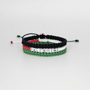 May include: Three braided bracelets in green, black, and white with red beads. The middle bracelet has white letter beads spelling out "PALESTINE".