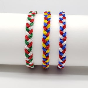 May include: Three braided bracelets in red, white, blue, and green colors. The bracelets are made of woven cord and are a popular style of friendship bracelet.