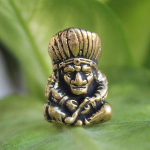 May include: A small gold-colored figurine of a Native American man wearing a feathered headdress and sitting cross-legged. The figurine is holding a pipe in his hand.