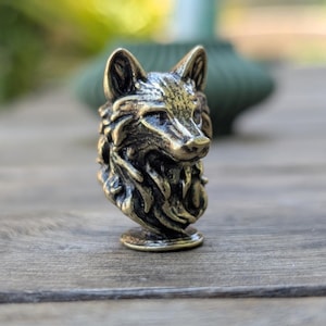 May include: A detailed bronze sculpture of a wolf's head, with a textured fur design. The sculpture is mounted on a small, round base.
