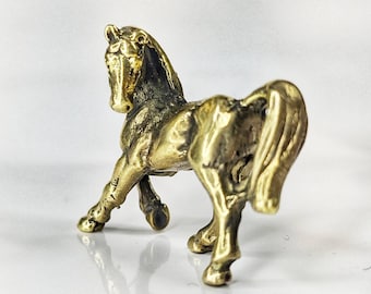 May include: A small, detailed brass horse figurine. The horse is posed with its head turned, and its tail is flowing. The figurine has a polished, antique finish. The horse is a decorative item.