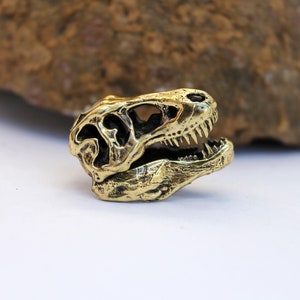 May include: A gold-colored metal dinosaur skull keychain. The skull is detailed with teeth and eye sockets.