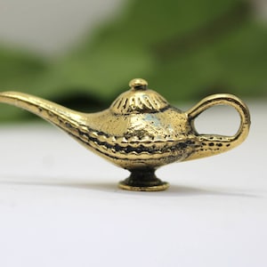 May include: A small, gold-colored genie lamp with a detailed design. The lamp has a spout and a handle.