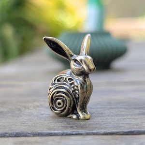 May include: A small, bronze sculpture of a rabbit with intricate, swirling patterns on its body. The rabbit is sitting upright with its ears perked up.