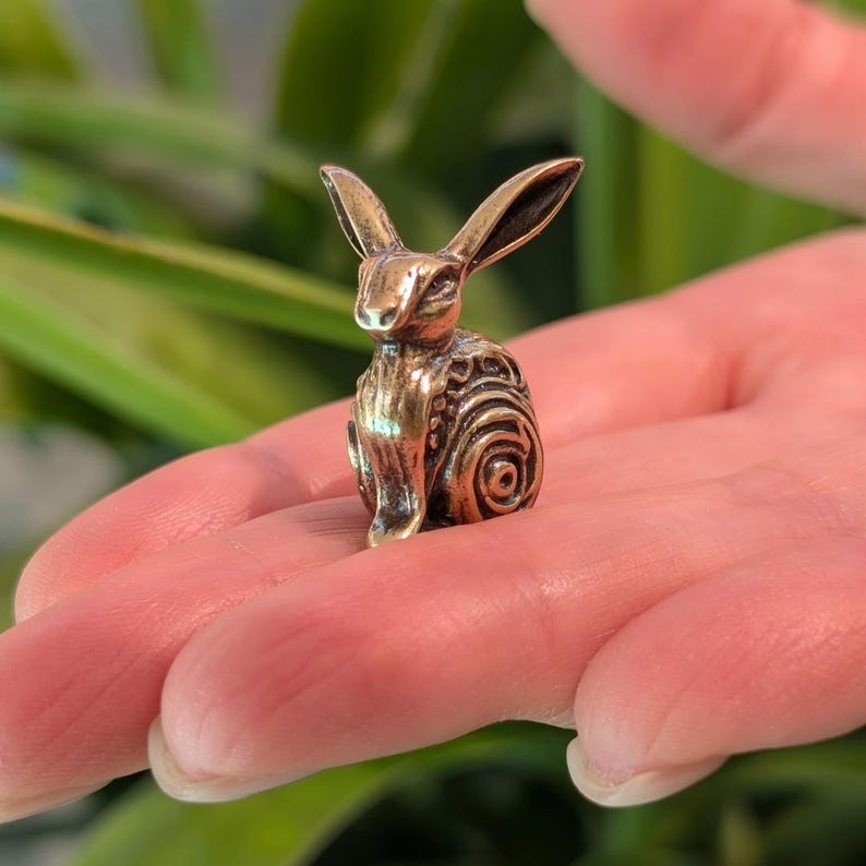 May include: A small, bronze sculpture of a rabbit with intricate details. The rabbit is sitting upright with its ears perked up.