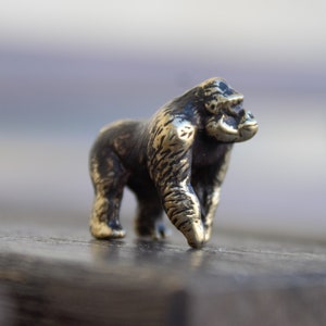 K&ouml;nnte beinhalten: Eine kleine, detaillierte Bronzefigur eines Gorillas. Die Figur steht auf einer dunklen Holzoberfl&auml;che.