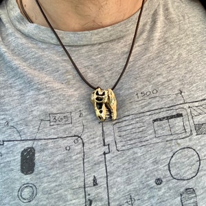 May include: A gold-colored dinosaur skull pendant on a brown leather cord necklace.