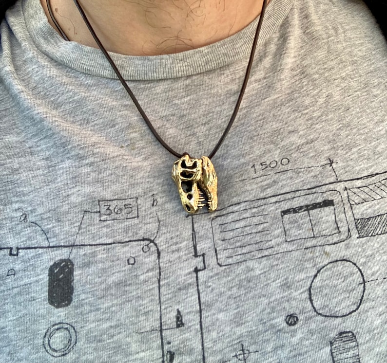May include: A gold-colored dinosaur skull pendant on a brown leather cord necklace.