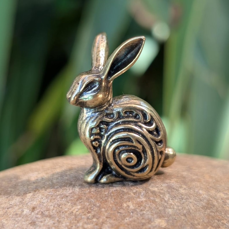 May include: A small, detailed bronze rabbit figurine with a swirling pattern on its body. The rabbit is sitting upright with its ears perked up.