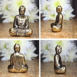 May include: A small, gold-colored, metal statue of a seated Buddha. The statue is in a meditative pose with hands resting in the lap. The statue is about 2 inches tall.
