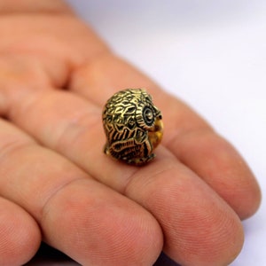 May include: A small, gold-colored owl figurine with intricate details. The owl is perched on a finger, showcasing its size.