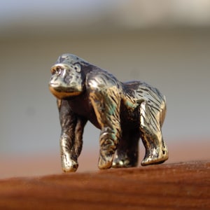 K&ouml;nnte beinhalten: Eine kleine, goldfarbene Metallfigur eines Gorillas. Der Gorilla steht auf allen Vieren und hat eine detaillierte, strukturierte Oberfl&auml;che.