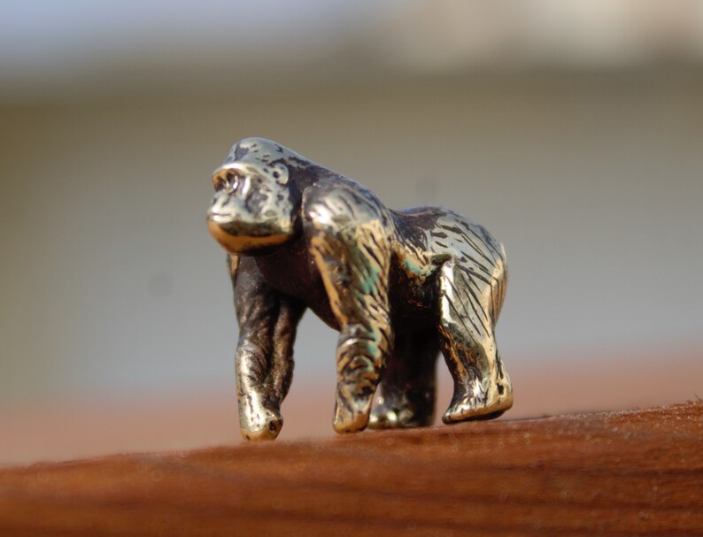K&ouml;nnte beinhalten: Eine kleine, goldfarbene Metallfigur eines Gorillas. Der Gorilla steht auf allen Vieren und hat eine detaillierte, strukturierte Oberfl&auml;che.
