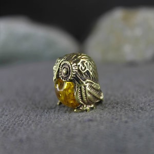 May include: A small, gold-colored owl figurine with a detailed design. The owl's eyes are made of amber.