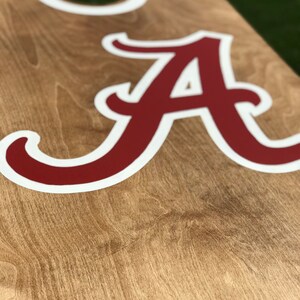May include: A wooden cornhole board with a light brown finish. The board features a large, red letter "A" with a white outline, and a white-rimmed hole. The design is likely for a college sports team.
