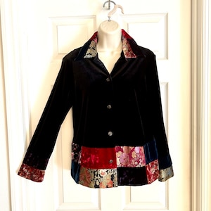 May include: Black velvet jacket with long sleeves and a patchwork design at the hem and cuffs. The collar and cuffs feature a patterned fabric with red, gold, and green accents. The jacket has decorative buttons.