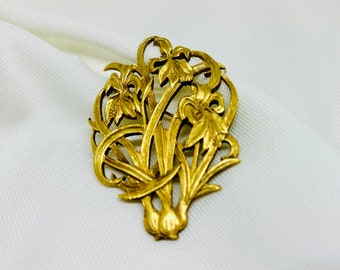 Peut inclure: Broche dorée représentant un motif floral stylisé. La broche représente un bouquet de fleurs d'iris avec des pétales et des feuilles détaillés. Le métal a un aspect légèrement vieilli, ajoutant à son charme vintage.
