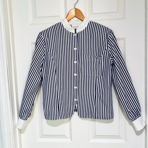 May include: A black and white striped button-down shirt with a white collar and cuffs. The long-sleeved shirt has a single pocket on the chest and is hanging on a wooden hanger.