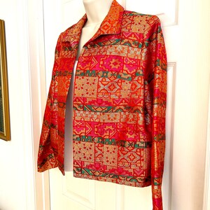 May include: A vibrant, open-front jacket with a striking geometric pattern in shades of red, orange, gold, and green. The jacket features a collared neckline and long sleeves, showcasing a bold, eye-catching design.