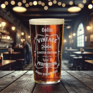May include: A clear glass pint glass with a brown liquid inside. The glass is engraved with the text "Colin Vintage 2006 Limited Edition Aged to Perfection Happy 18th Birthday".