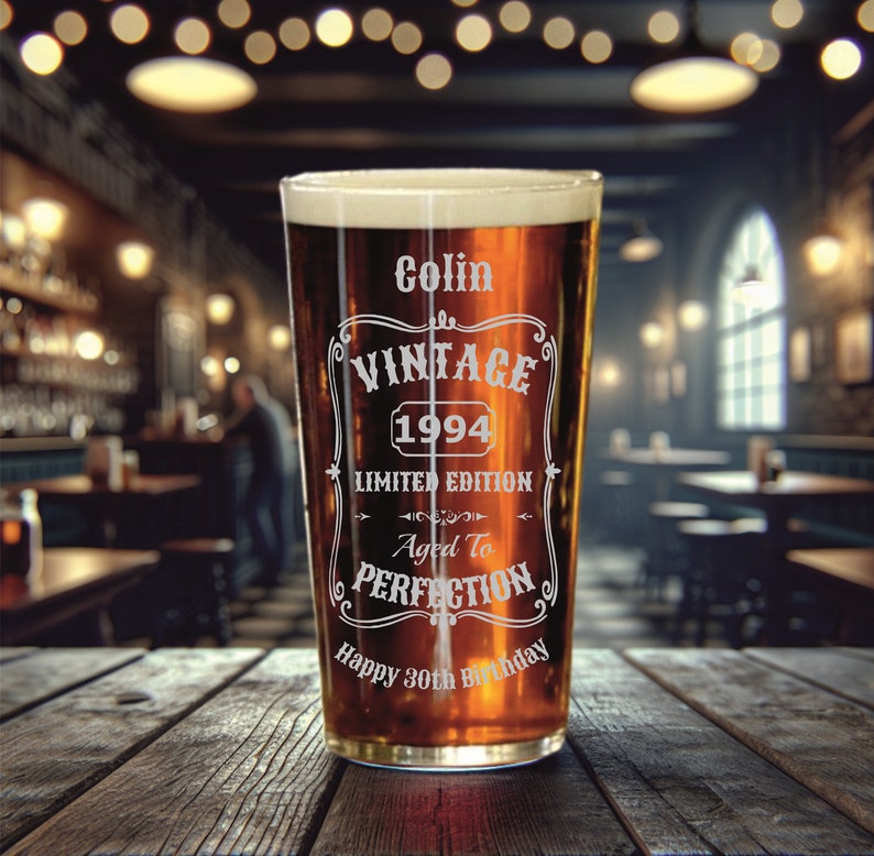 May include: A clear glass pint glass with a brown liquid inside. The glass has an etched design that says "Colin Vintage 1994 Limited Edition Aged to Perfection Happy 30th Birthday".