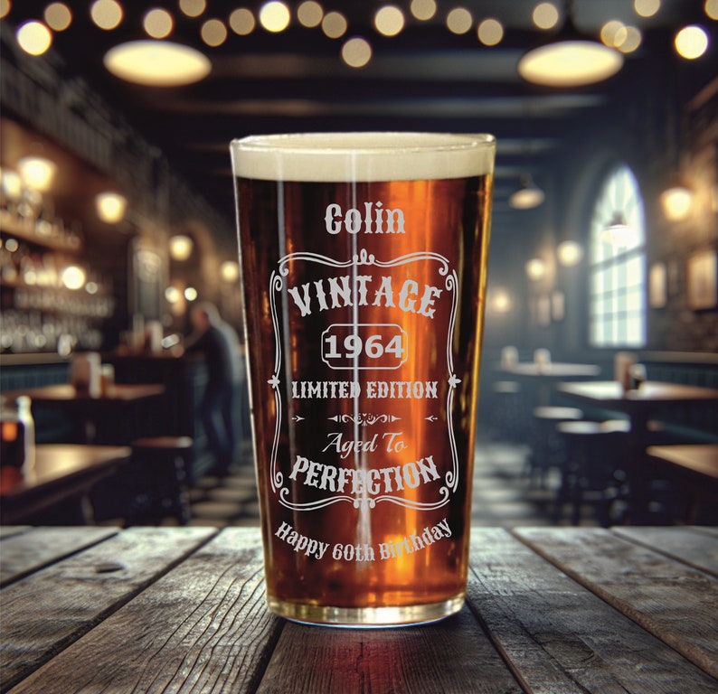May include: A clear glass pint glass with a brown liquid inside. The glass has an etched design that says "Colin Vintage 1964 Limited Edition Aged to Perfection Happy 60th Birthday".