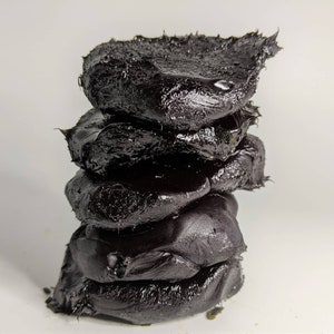 May include: A stack of four black, irregularly shaped, sticky, and gooey pieces of tar or asphalt.
