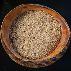 May include: A wooden bowl filled with light brown wood shavings. The bowl has a natural, organic shape with a dark brown rim and a lighter brown interior. The wood shavings are finely shredded and fill the bowl.