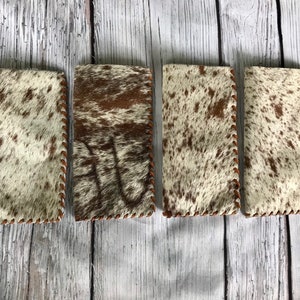 May include: Four brown and white cowhide leather phone cases with brown stitching.