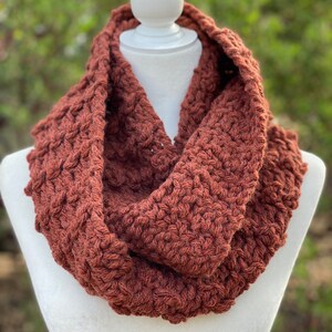 May include: A brown crocheted infinity scarf. The scarf is made with a chunky yarn and has a textured stitch pattern.