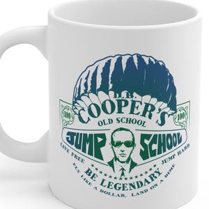 以下が含まれることがあります： 白のセラミックマグカップ。緑と青のグラフィックが特徴で、「COOPER'S OLD SCHOOL JUMP SCHOOL」の文字とパラシュートのイラスト、サングラスをかけた男性が描かれています。追加のテキストには「LIVE FREE, FLY LIKE A DOLLAR, BE LEGENDARY, LAND ON A DIME, JUMP HARD」と書かれています。