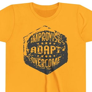 Pode incluir: Camiseta amarelo mostarda com um gráfico preto desgastado. O gráfico é um hexágono com as palavras "IMPROVISE, ADAPT, OVERCOME" em uma fonte de estilo vintage. A camiseta é feita de um material macio.