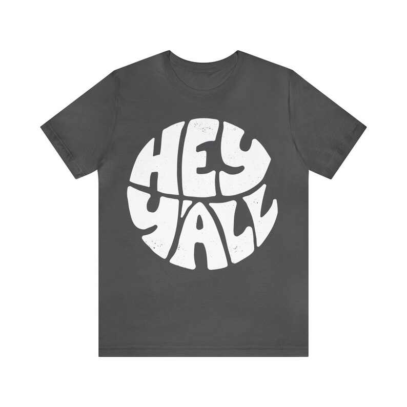 Pu&ograve; includere: Una maglietta grigio scuro con una grafica circolare bianca che dice "Hey Y'all" in un font retr&ograve;.
