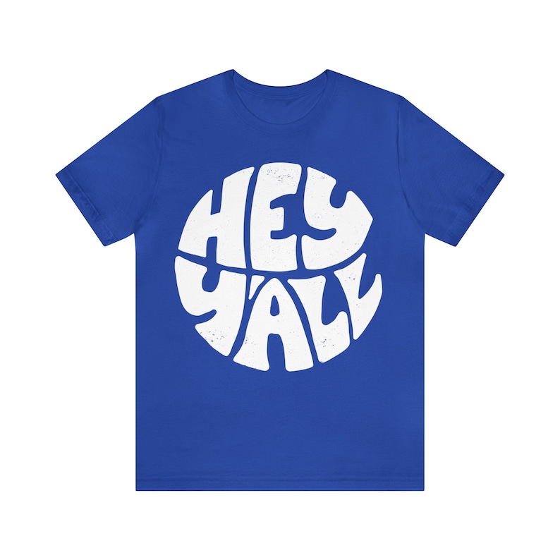 Pu&ograve; includere: Una t-shirt blu reale con una grafica circolare bianca che dice "Hey Y'all" in un font retr&ograve;.