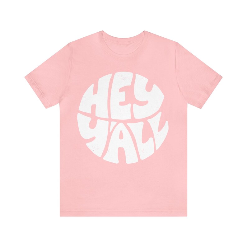 Pu&ograve; includere: Maglietta rosa con una grafica circolare bianca che dice "Hey Y'all" in un font retr&ograve;.