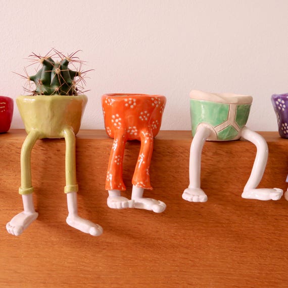 A handmade ceramic planter with little sculpted legs — absurdly charming pottery that straddles the line between functional plant pot and weird shelf art.