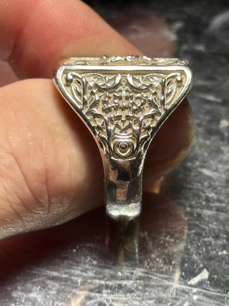 Pode incluir: Um anel de prata com um design intrincado e detalhado. O anel tem uma parte superior de forma quadrada com um padr&atilde;o floral.