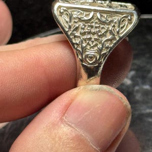 Pode incluir: Um anel de prata com um design intrincado e detalhado. O anel tem uma parte superior quadrada com um padr&atilde;o floral.