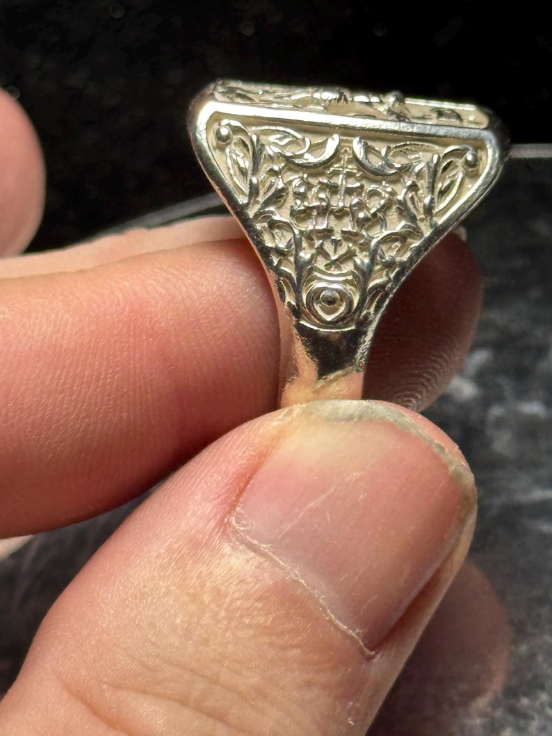 Pode incluir: Um anel de prata com um design intrincado e detalhado. O anel tem uma parte superior quadrada com um padr&atilde;o floral.