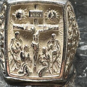 Pode incluir: Um anel de prata com um design detalhado que apresenta um crucifixo e figuras. O anel tem a inscri&ccedil;&atilde;o "INRI" na cruz.