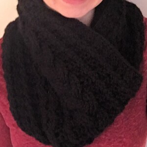 Peut inclure: Une femme portant une écharpe en tricot noire infinie. L'écharpe est épaisse et présente un motif en tricot torsadé.