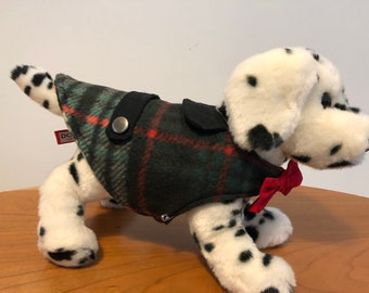 May include: A white and black Dalmatian dog wearing a green, red, and black plaid coat with a black collar and a red bow tie.
