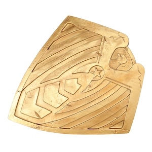 May include: A gold-colored shield with a star in the center and a decorative pattern. The shield has a worn, textured surface.