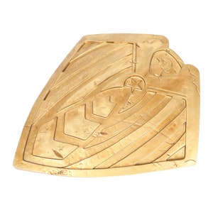 May include: A gold-colored shield with a star in the center and a decorative pattern. The shield is made of a textured material and has a slightly worn appearance.