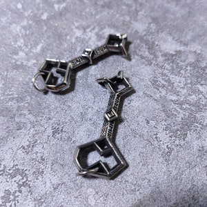 May include: Two silver metal keys with intricate designs. The keys are on a gray textured surface.