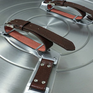 May include: Close-up of a silver metal shield with three brown leather straps. The straps are attached to the shield with metal buckles and rivets.