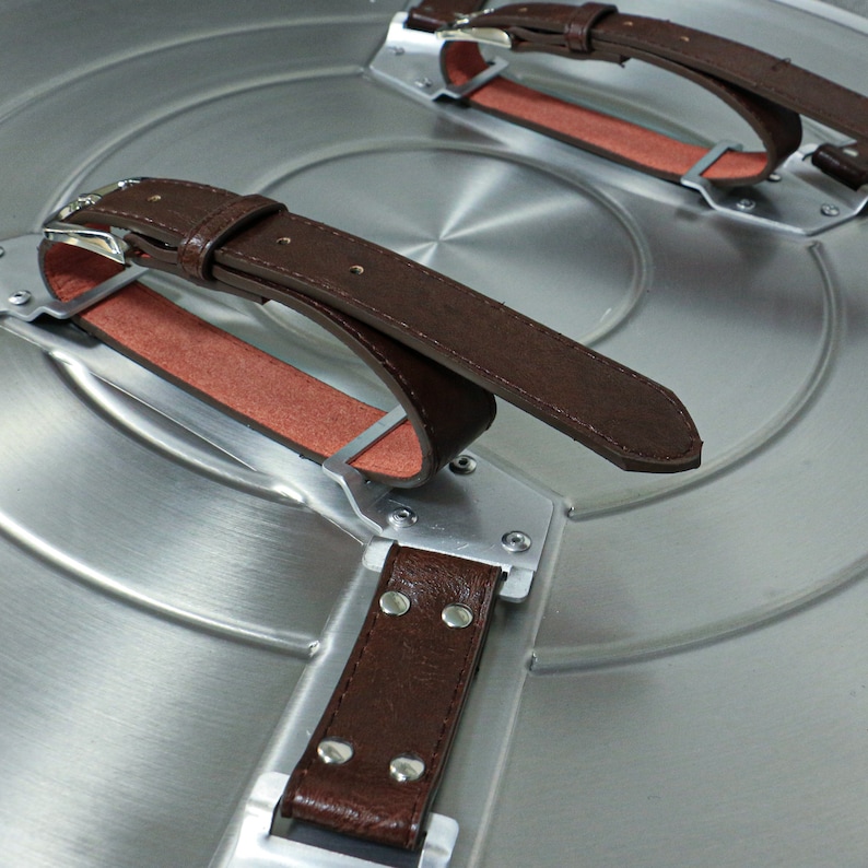 May include: Close-up of a silver metal shield with three brown leather straps. The straps are attached to the shield with metal buckles and rivets.