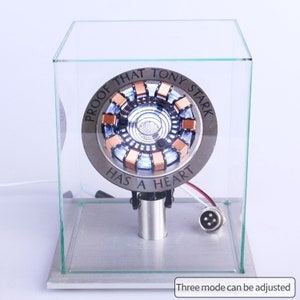 May include: A glass display case with a silver and copper-colored Iron Man Arc Reactor replica inside. The replica has a white light and the text "Proof that Tony Stark has a heart".
